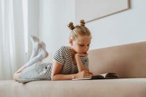 The girl is relaxing on the sofa while reading a book